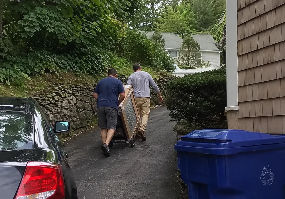 Two installers moving a boxed air conditioning unit up a driveway