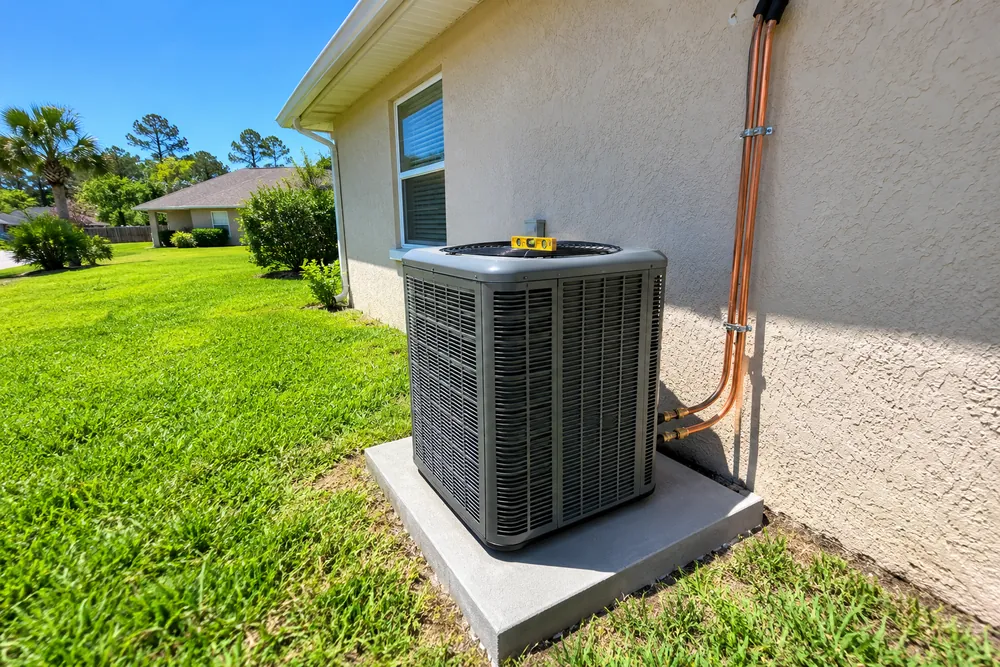 Newly installed outdoor heat pump condenser on a concrete pad with copper line set beside a Florida home